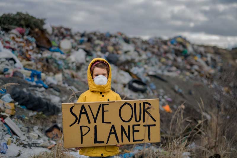 Child holding a sign saying "Save Our Planet" sign standing in front of a landfill